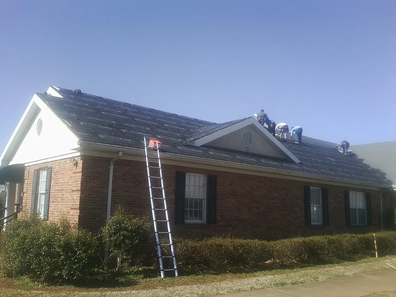 Crew tearing shingles off a brick ranch roof with a ladder set — Emergency Roof Repair work by our crew in Glastonbury