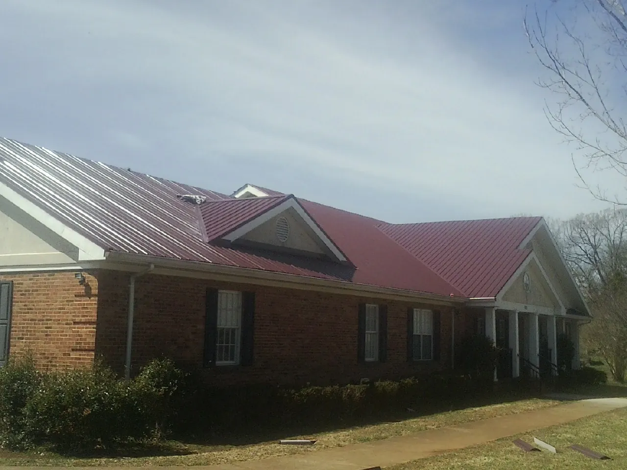 Red metal roof with gabled entries on a long brick building, from a Hail Damage Roof Repair job in Glastonbury