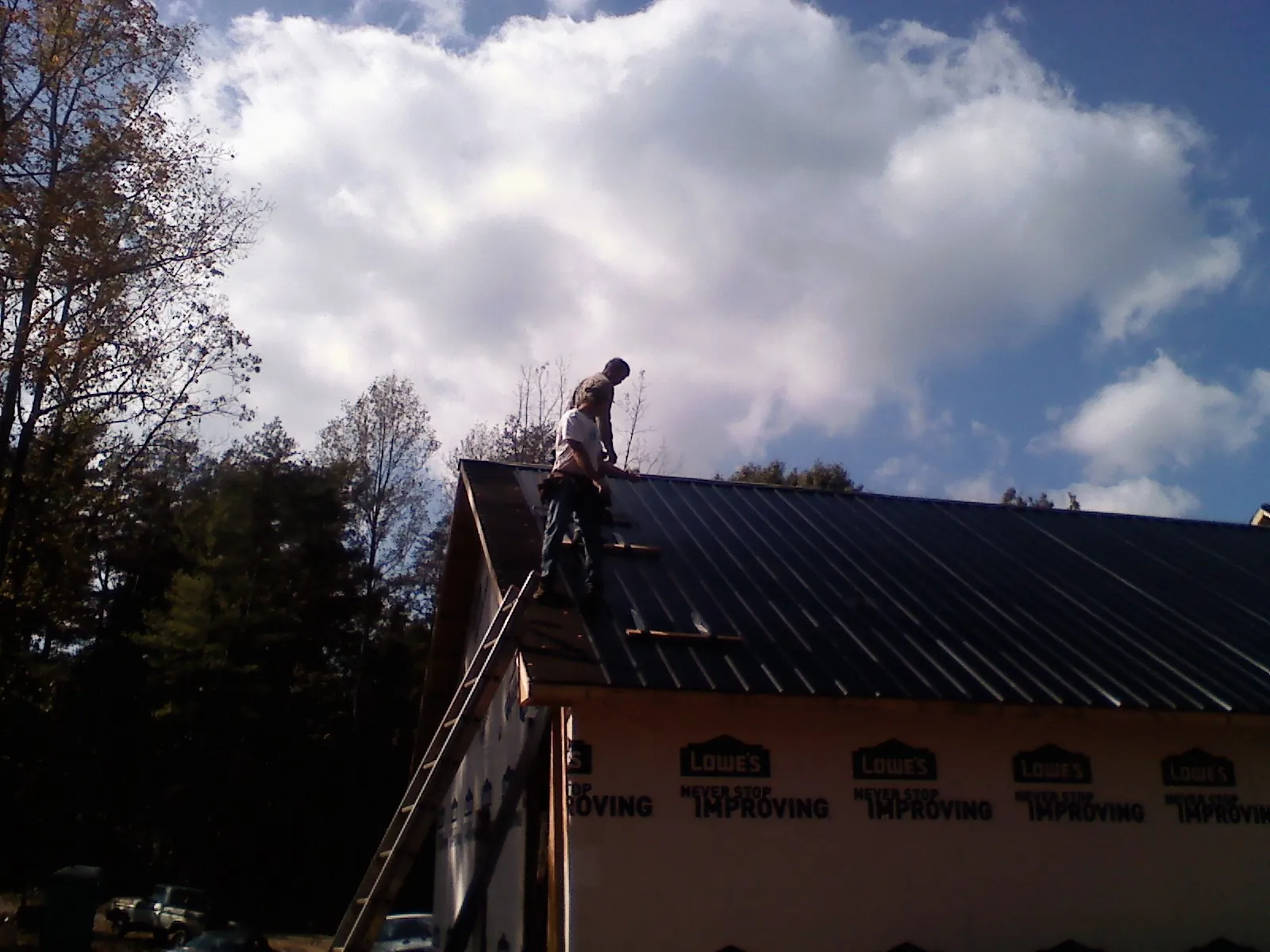 Roofer fastening dark metal panels high against a cloudy sky, from a Roof Inspection job in Glastonbury