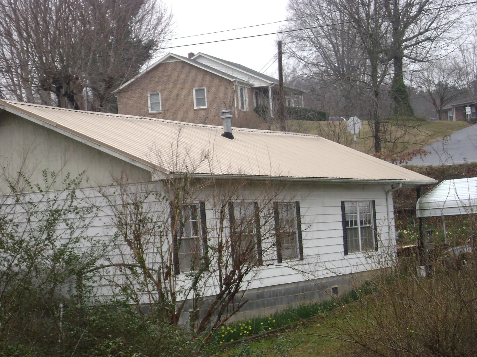 Tan metal roof on a white sided house set into a hillside — Commercial Roofing by Roofing Brothers in Glastonbury