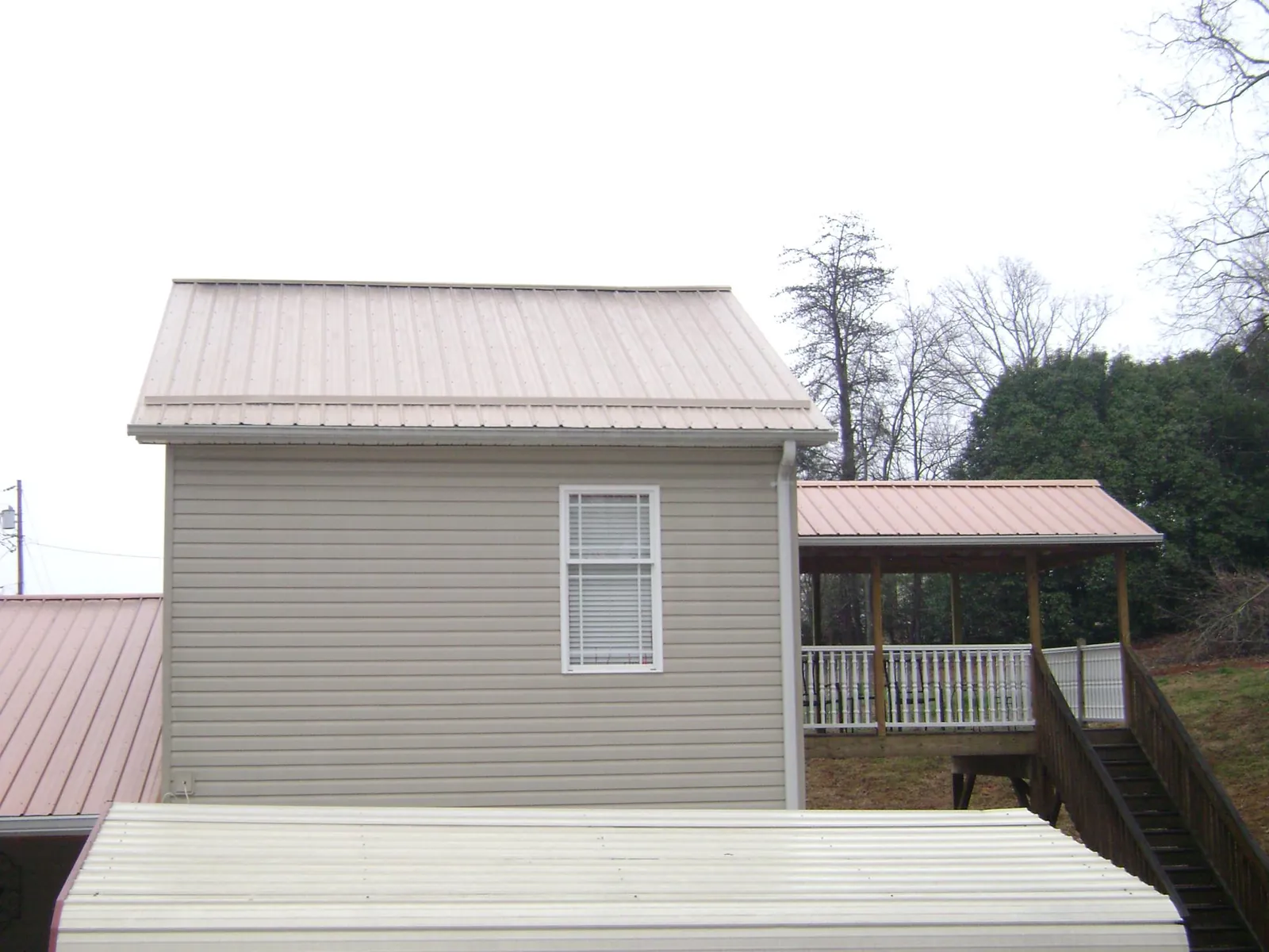 Tan metal roofs on a two story addition and attached porch, from a Roof Replacement job in Glastonbury